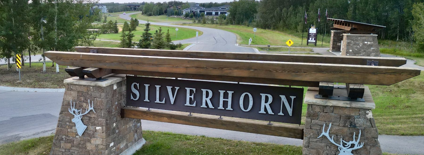 The Silverhorn entrance: a heavy timber beam on two stone piers, each carrying a stag in relief, with the community road running behind it.